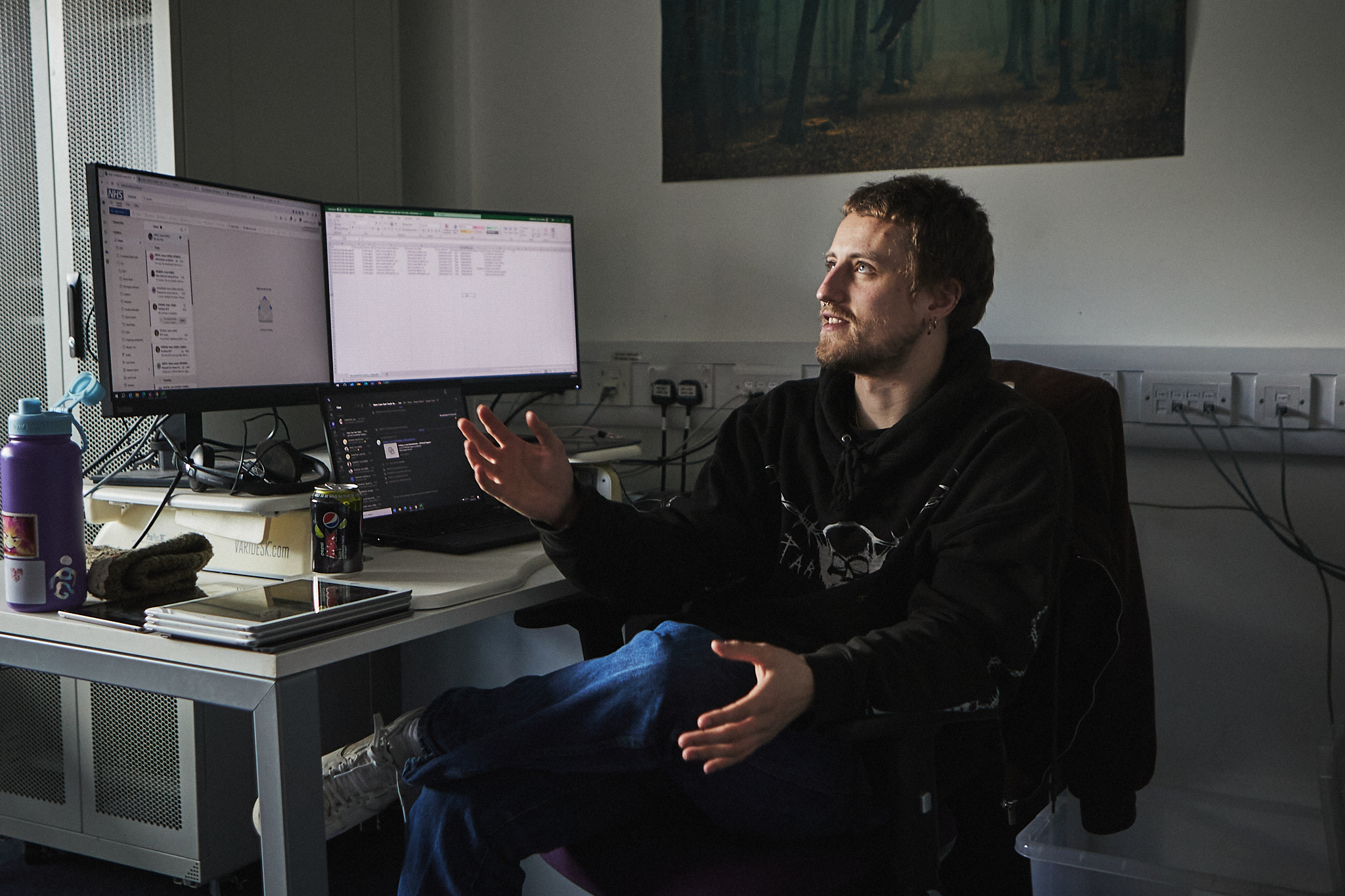 One of the Data and Analytics team - a young, white man sat a desk in front of a double computer screen talking to someone out of shot