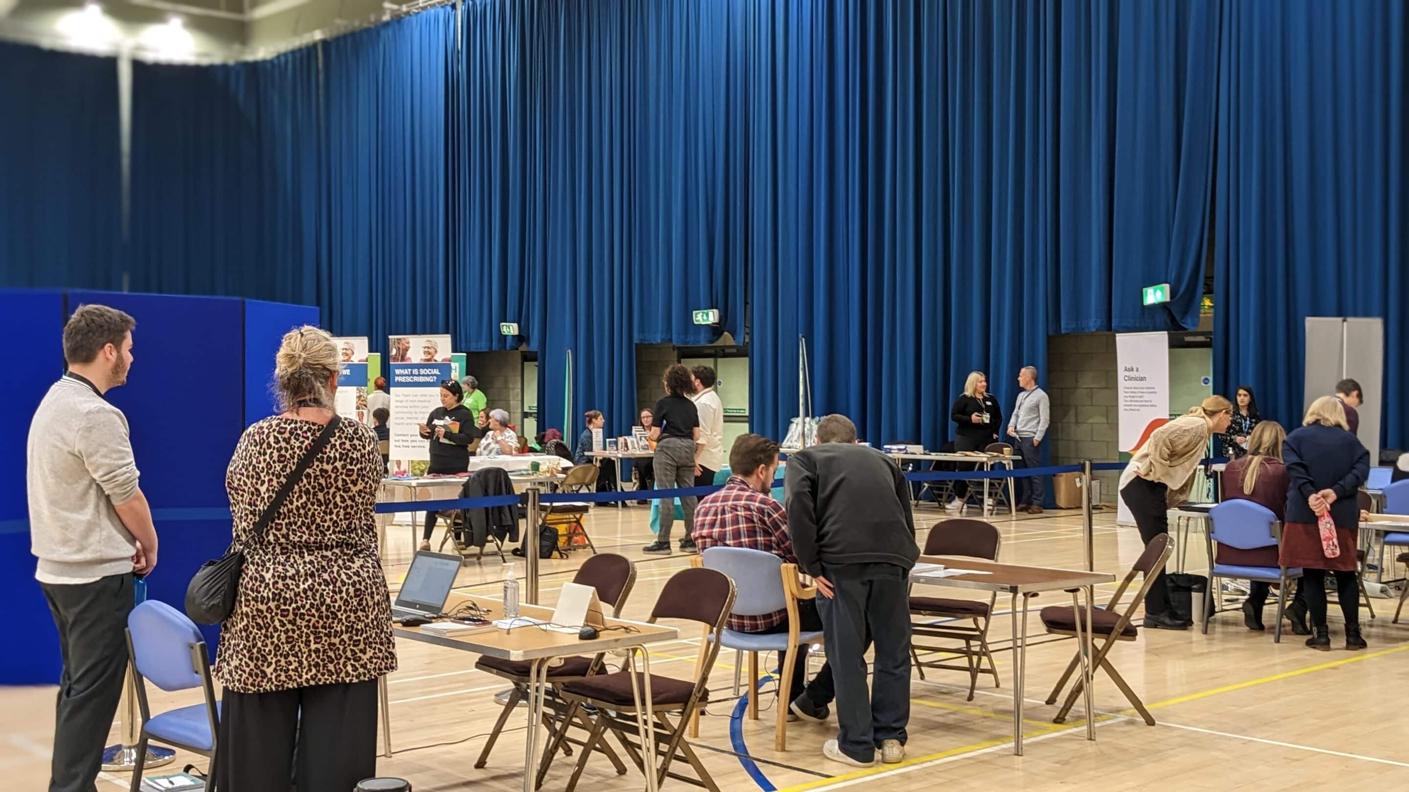 A sports hall where a Community Appointment Day is being held with seats laid out for people attending. The evaluation was commissioned to understand and learn from these events.