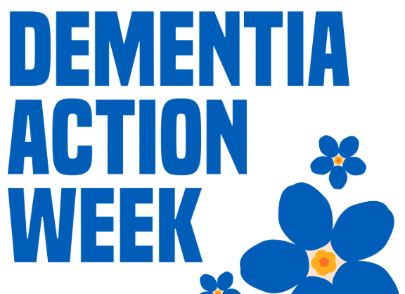 dementia action week alzheimers uk Photo of two white women outside with trees in the background. stood next to each other and smiling towards the camera. The woman on the left has long hair and the woman on the right has a short bobbed hair cut.